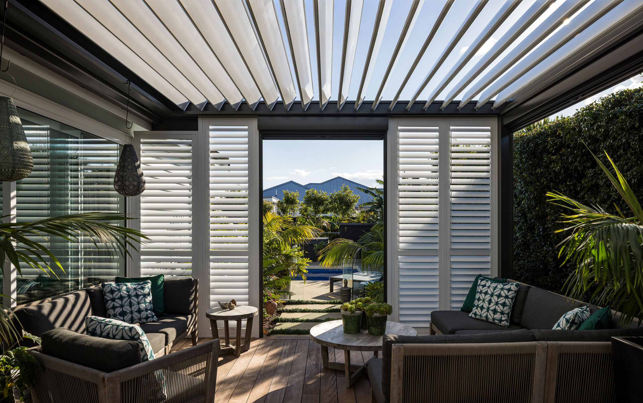Operable louvre roof over outdoor seating area with shutters and garden view